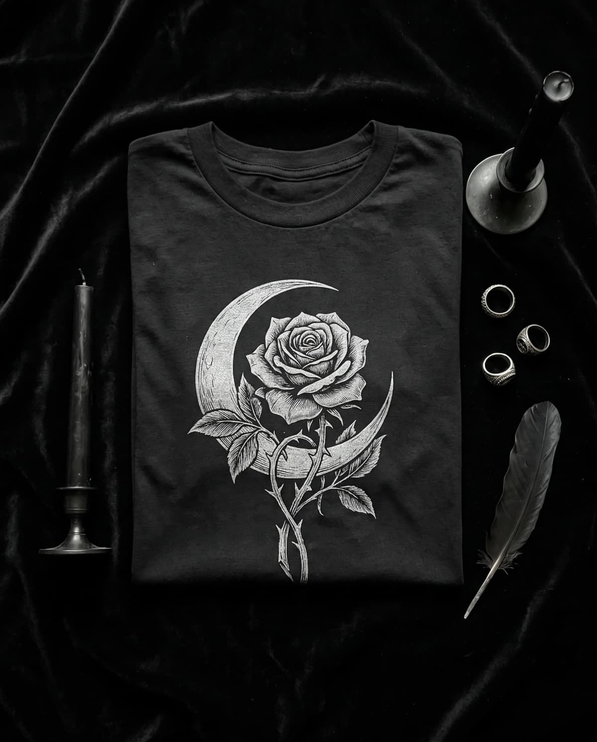 Schwarzes T-Shirt mit Rosen-und-Mondsichel-Radierung auf Samt neben Kerzen und Silberringen