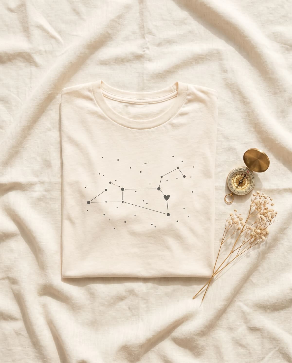 Cremefarbenes T-Shirt mit Sternbild-Print aus Punkten und Linien mit kleinem Herz, daneben Kompass