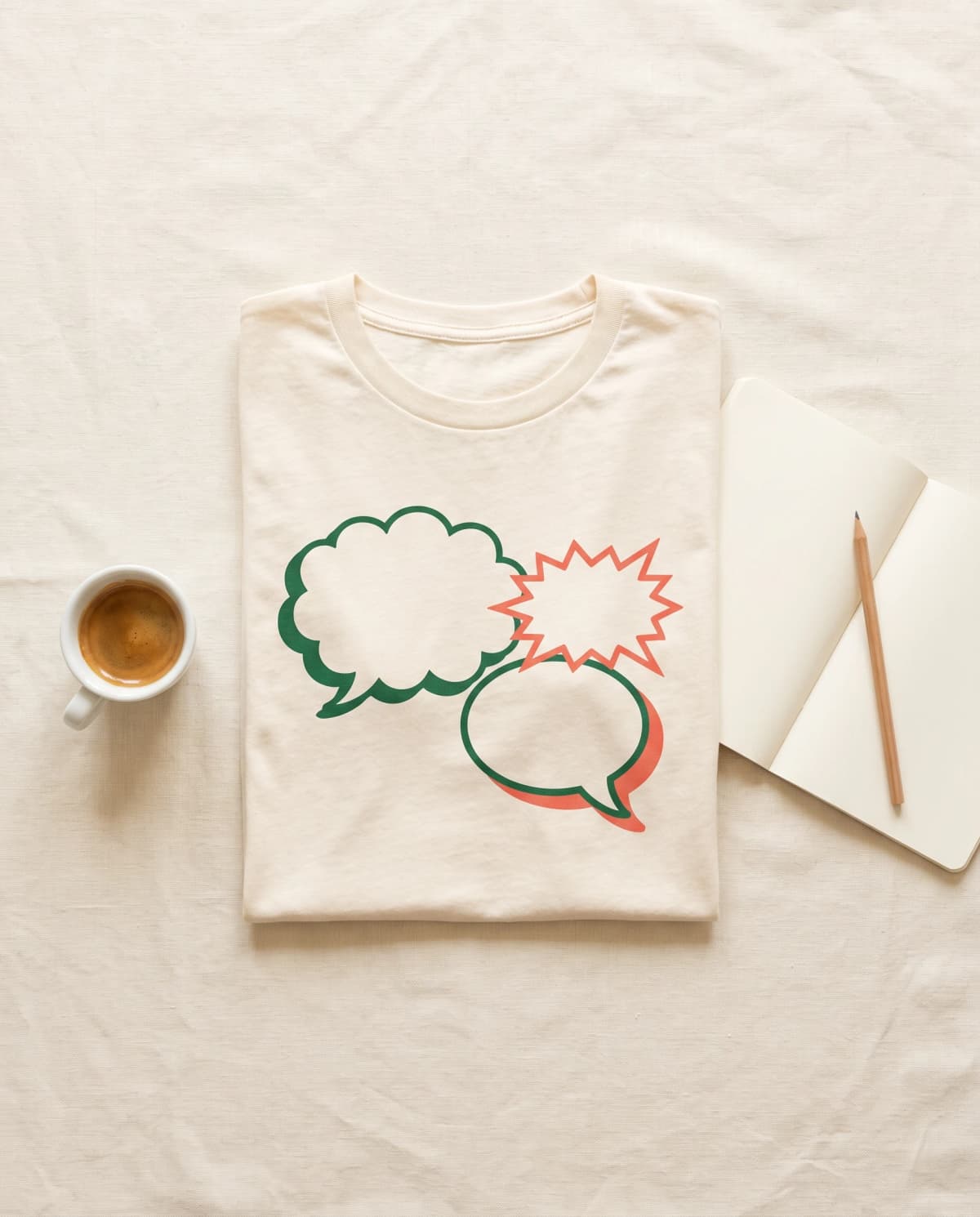 Cremefarbenes T-Shirt mit Sprechblasen-Grafik-Print, daneben Notizbuch, Bleistift und Espresso