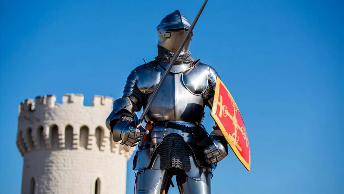 Ritter in glänzender Plattenrüstung mit Schwert und rotem Schild vor einem Burgturm und blauem Himmel